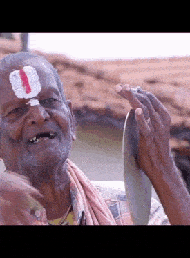 an elderly man with a red and white flower on his forehead is holding a piece of paper in his hand .