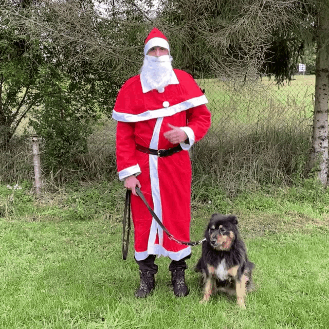 a man in a santa claus costume stands next to a dog on a leash