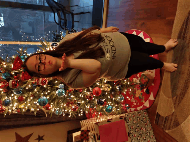 a woman standing in front of a christmas tree wearing a shirt that says " stay indoors "