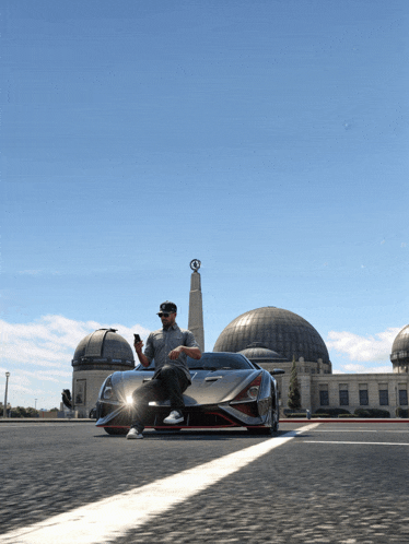 a man is sitting in front of a sports car looking at his phone