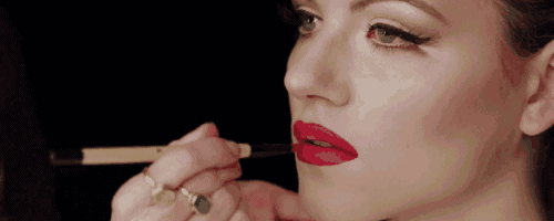 a woman applies red lipstick to her lips with a brush