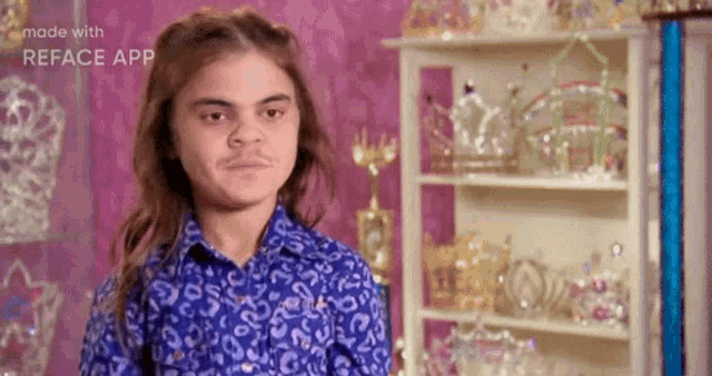 a young boy with long hair and a mustache is standing in front of a shelf filled with trophies .