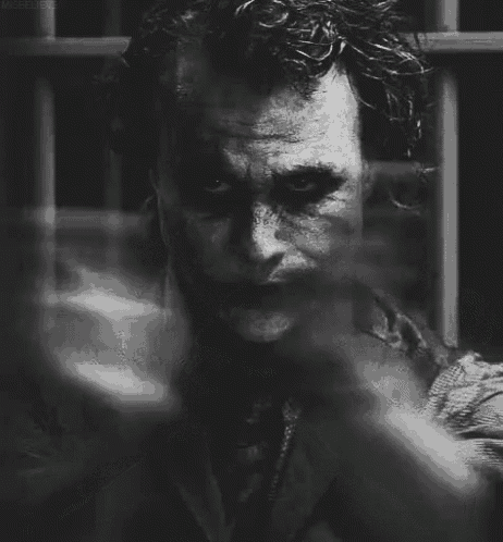 a black and white photo of the joker smoking a cigarette in a jail cell .