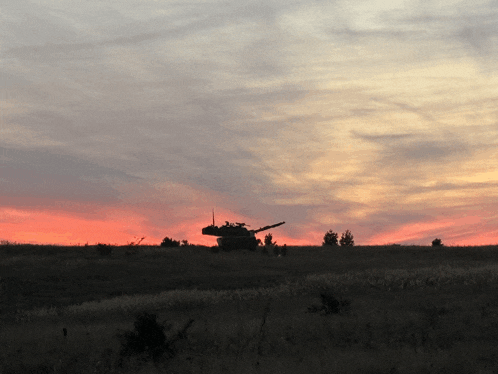 a tank is silhouetted against a sunset sky in a field