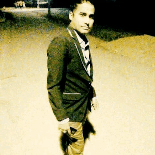 a young man in a suit and tie is standing on a dirt road at night .