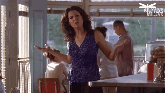 a woman in a blue tank top is standing in a diner holding a cigarette .