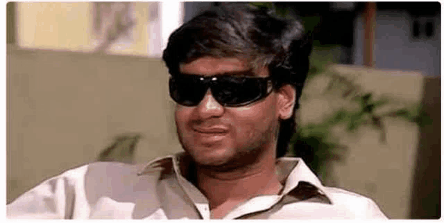 a man wearing sunglasses and a white shirt is smiling and looking at the camera .