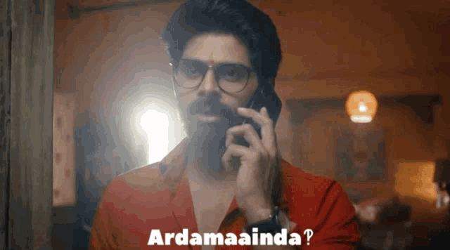 a man with glasses and a beard is talking on a cell phone and the words ardamaanda are above him