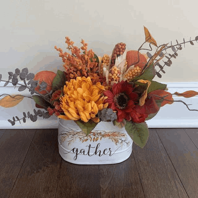 a white bucket filled with flowers and leaves is sitting on a wooden floor .