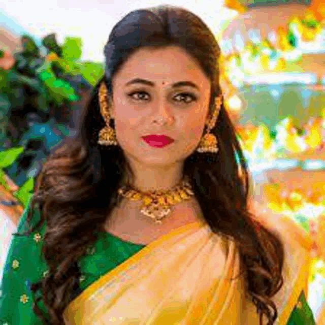 a woman wearing a yellow saree and a green blouse is standing in front of a building .