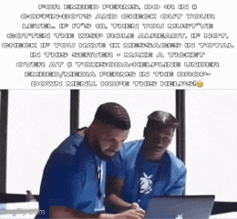 two men are sitting at a table with a laptop and one of them is wearing a blue shirt