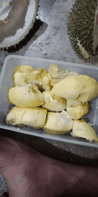 a person 's foot is next to a plastic container filled with durian