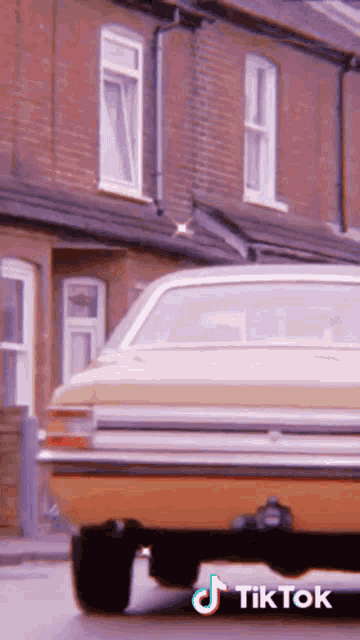 a yellow car is parked in front of a row of brick houses with tik tok written on the bottom right
