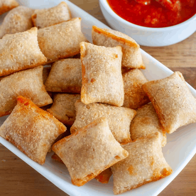 a white plate topped with pizza rolls next to a bowl of salsa