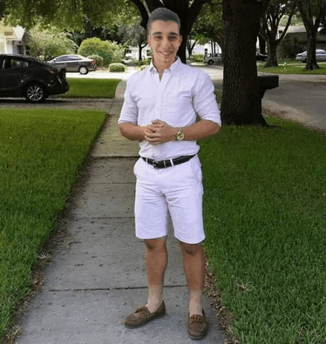 a man in a white shirt and white shorts is standing on a sidewalk