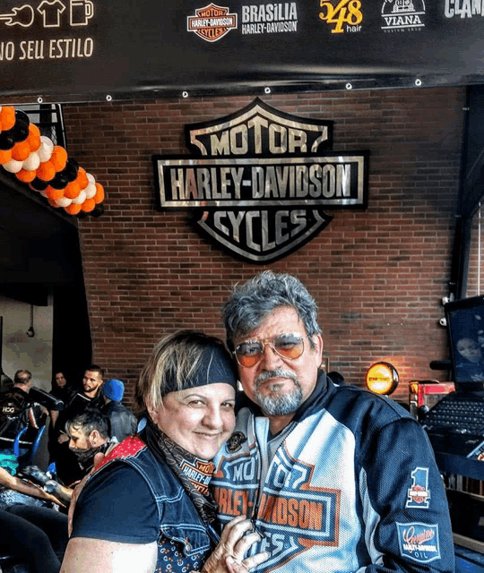 a man and woman are posing for a picture in front of a harley davidson sign