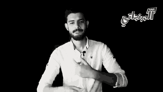 a man in a white shirt stands in front of a black background with arabic writing on it