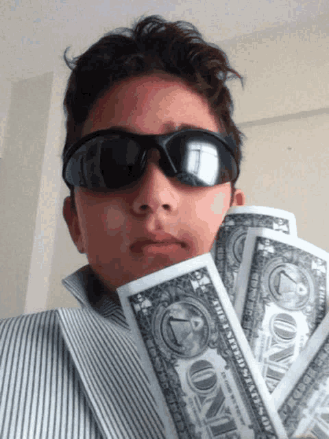 a young boy wearing sunglasses and holding a bunch of one dollar bills