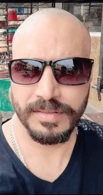a bald man with a beard and sunglasses is wearing a black shirt .