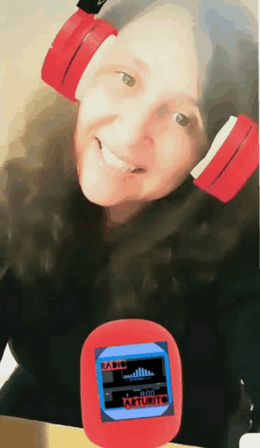 a woman wearing red headphones is smiling while holding a small red device that says radio arturito