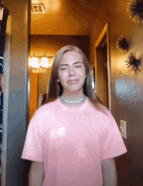 a girl in a pink t-shirt is crying in front of a mirror