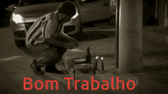 a black and white photo of a man kneeling in front of a car with bom trabalho written in red