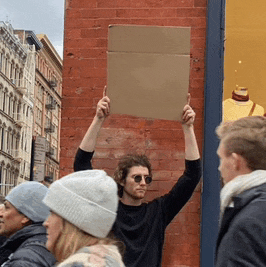 a man holding a cardboard sign in front of a brick wall