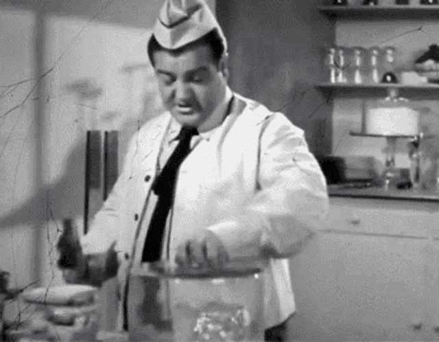 a black and white photo of a man in a chef 's hat and tie