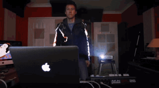 a man is standing in front of an apple laptop and an akai keyboard