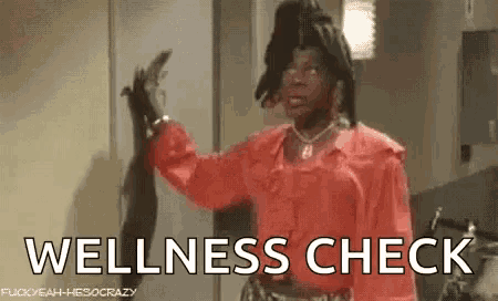 a man in a red shirt is standing in a kitchen holding a snake and the words `` wellness check '' .