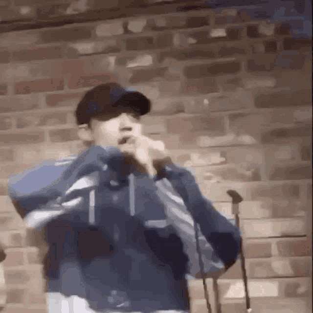 a man is singing into a microphone while wearing a hat and a blue jacket .