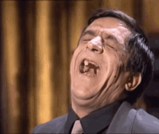 a man in a suit and tie is laughing with his eyes closed