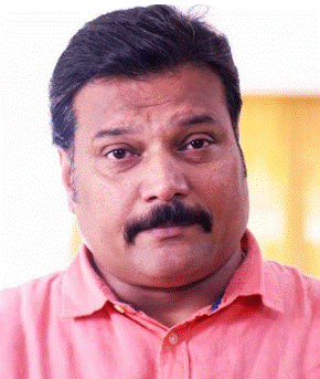 a man with a mustache and a pink shirt looks at the camera