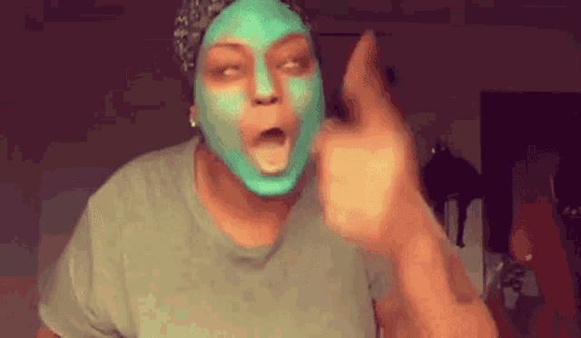 a woman wearing a green mask on her face is pointing her finger at the camera .
