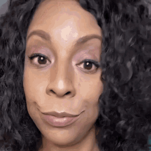 a woman with curly hair is smiling for the camera .