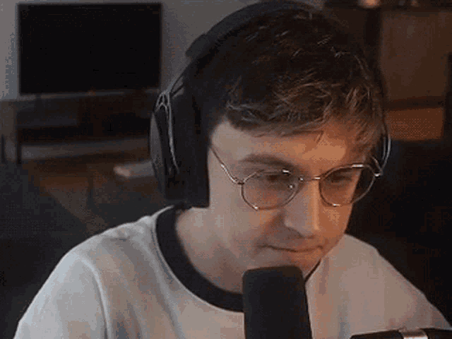 a young man wearing headphones and glasses is sitting in front of a microphone .