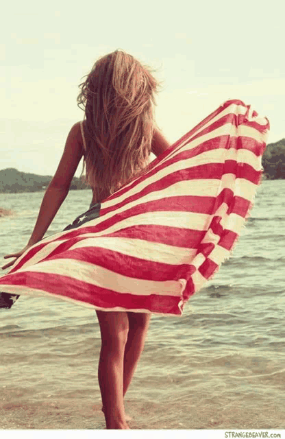 a woman is holding a red white and blue striped towel on the beach