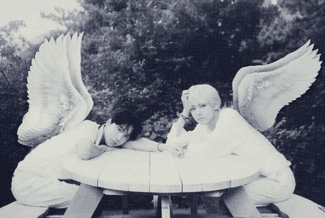 a black and white photo of two people with angel wings sitting at a table