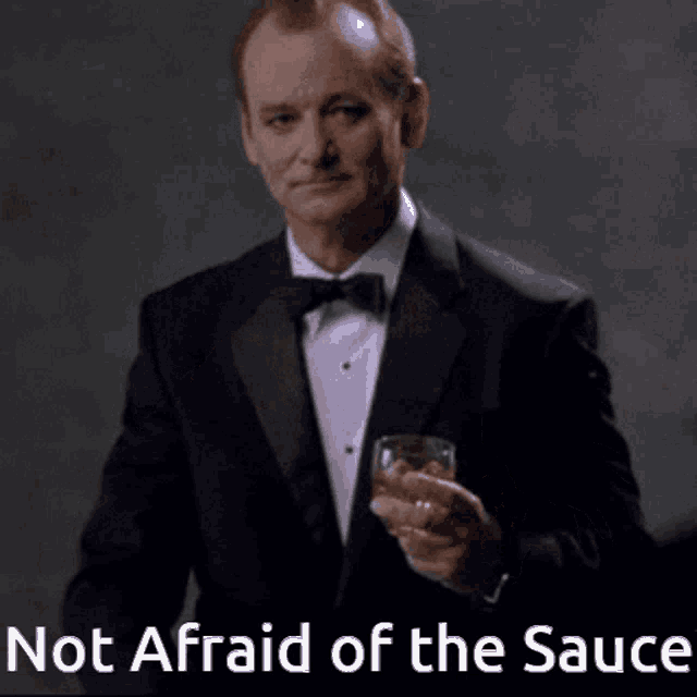a man in a tuxedo is holding a glass of whiskey and pointing at the words not afraid of the sauce