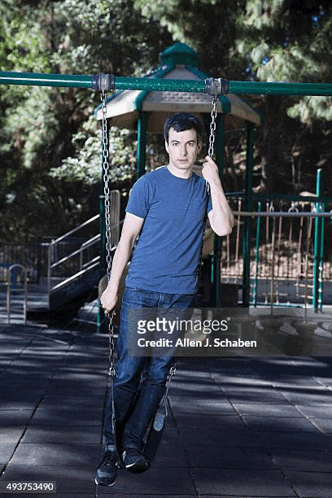 a young man is standing on a swing in a park