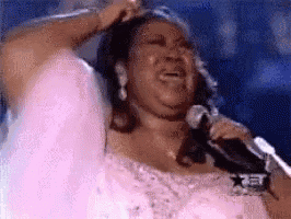 a woman in a pink dress is singing into a microphone while crying .