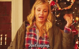 a woman in a plaid shirt is standing in front of a christmas tree and saying `` just saying '' .