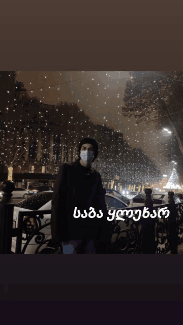 a man wearing a face mask is standing in front of a snowy street with a christmas tree in the background