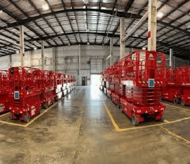 a row of red scissor lifts are parked in a large warehouse .