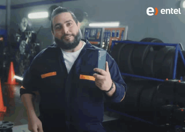 a man with a beard is holding a cell phone in front of a sign that says entel