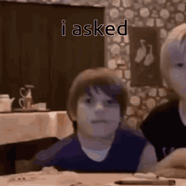 a young boy is sitting at a table with a pen in front of a sign that says i asked