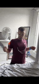 a man in a maroon nike shirt is standing in a bedroom holding a knife .