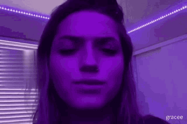 a close up of a woman 's face with her eyes closed under purple lights .