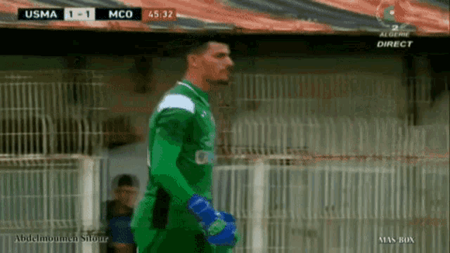 a soccer player in a green jersey stands in front of a fence during a match between usma and mco