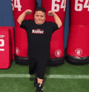 a young boy is flexing his muscles on a football field in front of a row of red dummies .